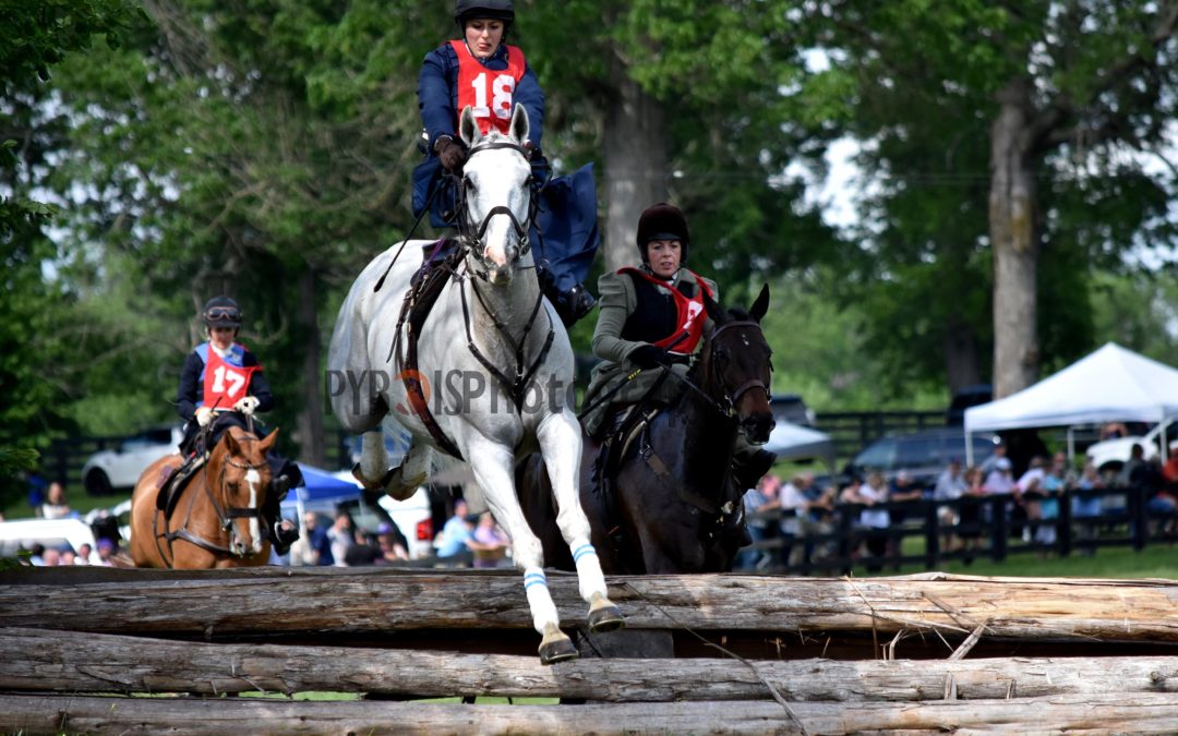 A woman jumping over a fence riding sidesaddle on a gray horse.